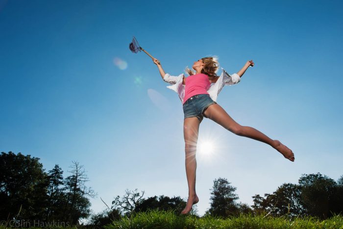Woman jumping against blue sky holding butterfly net by photographer Colin Hawkins