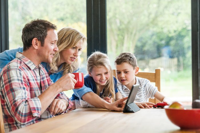 Lifestyle photography of a family with children sitting around a table inside & checking online using a smart device for Watsons fuel by Colin Hawkins