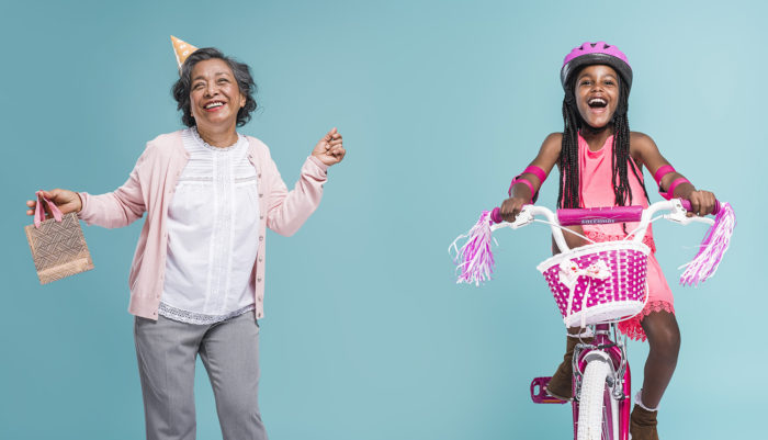 Azimo advertising portrait photography in Hawkeye Studio by Colin Hawkins of senior Filipino woman dancing with party hat & young girl riding pink bike against blue background