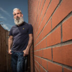 Business lifestyle portrait of senior man with grey beard leaning against a brick wall in an alleyway for Wessex Water by Colin Hawkins.