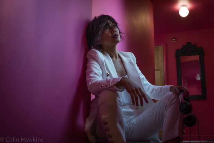 Asian woman in white suit slumped in pink interior by Colin Hawkins photography