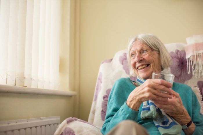 Campaign photography for Wessex Water by Colin Hawkins of a senior woman happily sitting near window holding a glass of water.