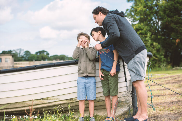 Father teaching sons how to thread fishing line onto a rod outside by photographer Colin Hawkins for Wessex Water