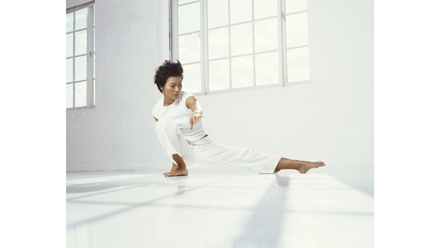 Asian woman exercising in white room with sunlight through windows doing Tai Chi by photographer Colin Hawkins